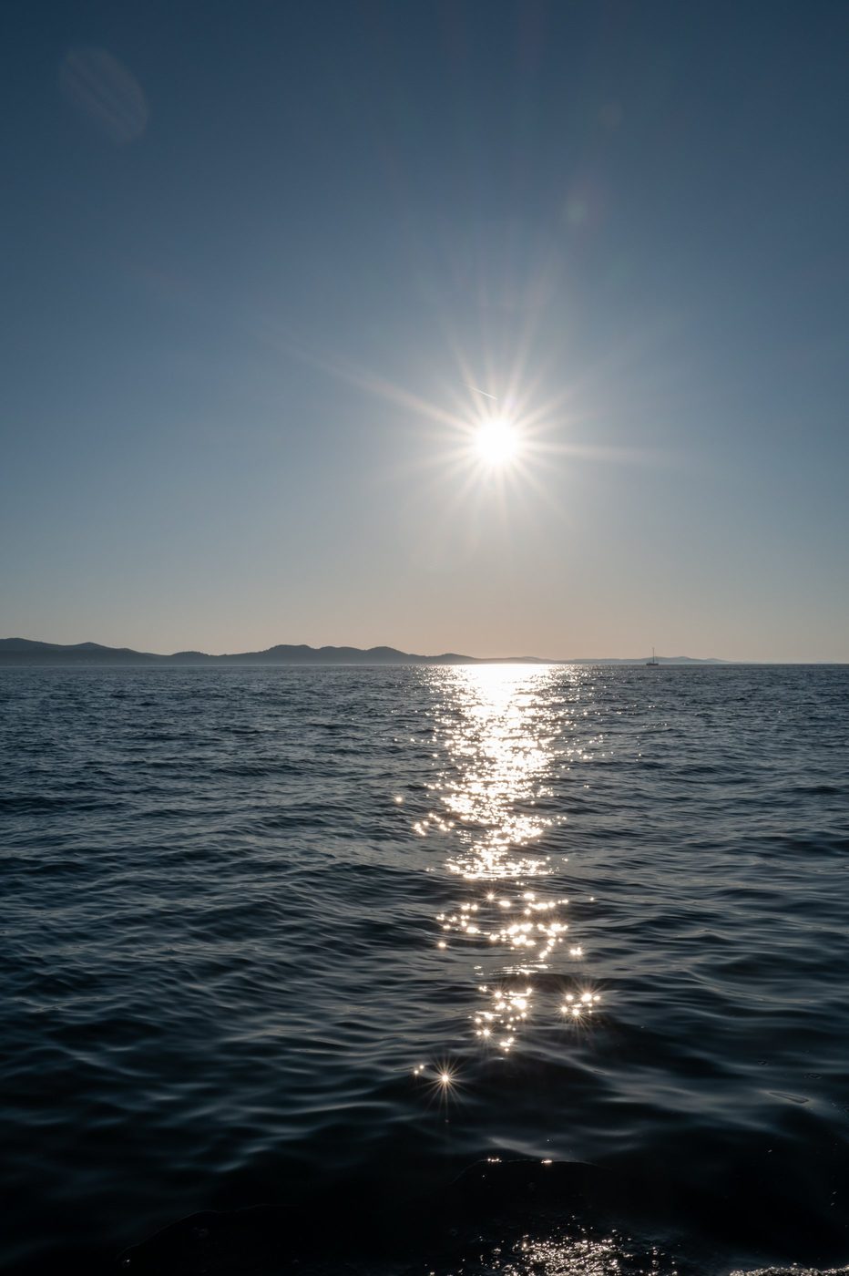 Shimmering reflection of the sun on the Adriatic, sailboat in the distance, Zadar