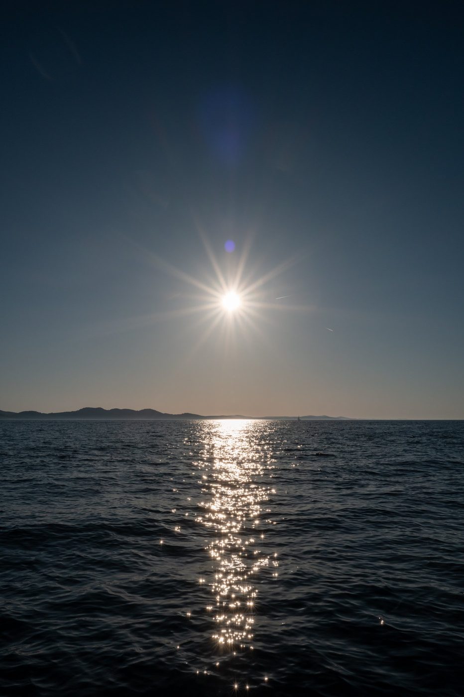 Sun star piercing a deep blue sky above the sea, Zadar
