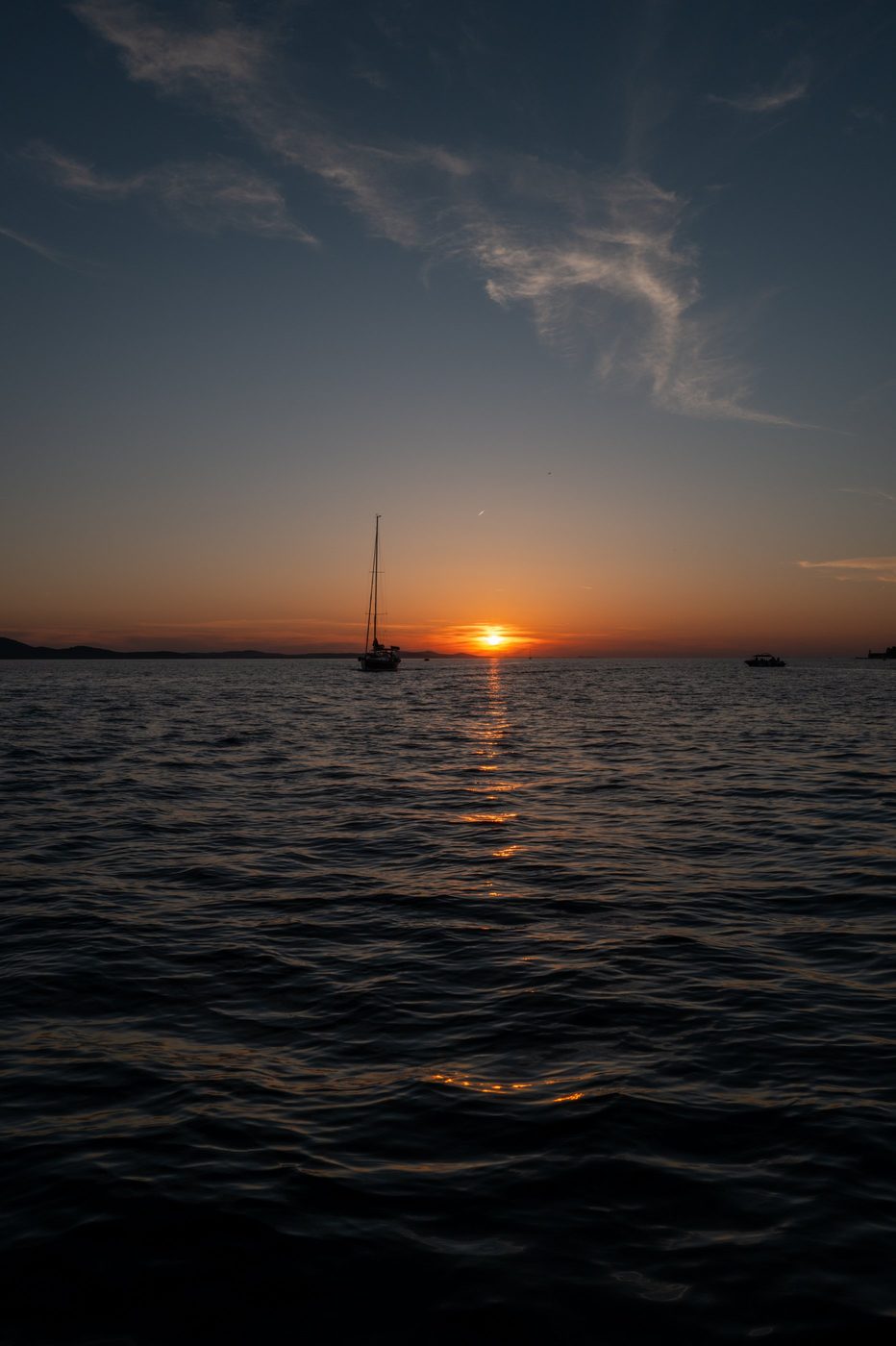Large sailboat anchored facing the sun's disk descending over the sea, Zadar