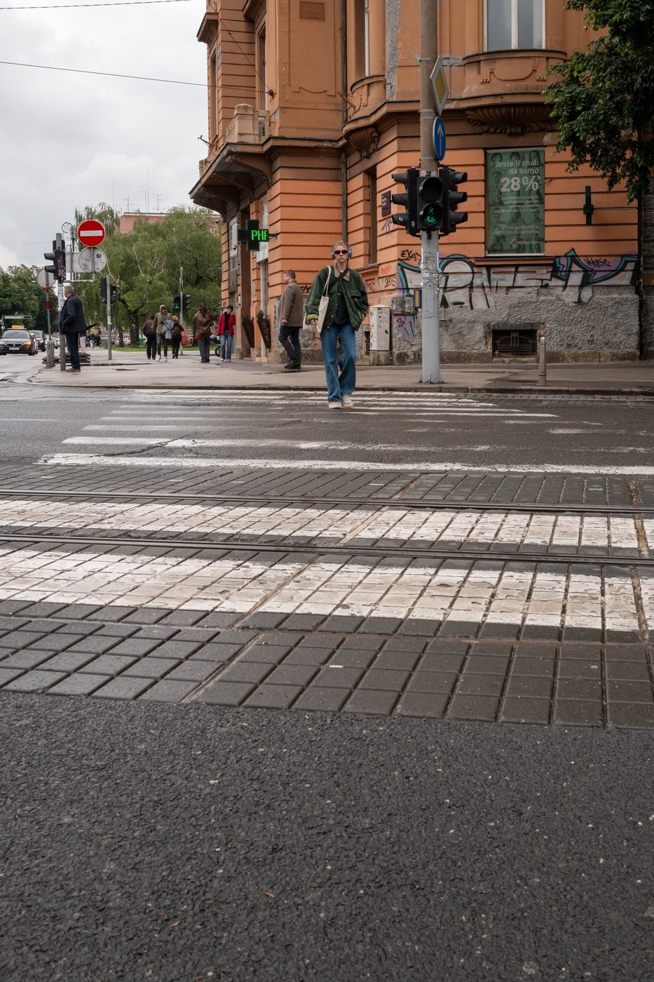 A pedestrian crossing in front of an ornate façade covered in graffiti, Zagreb