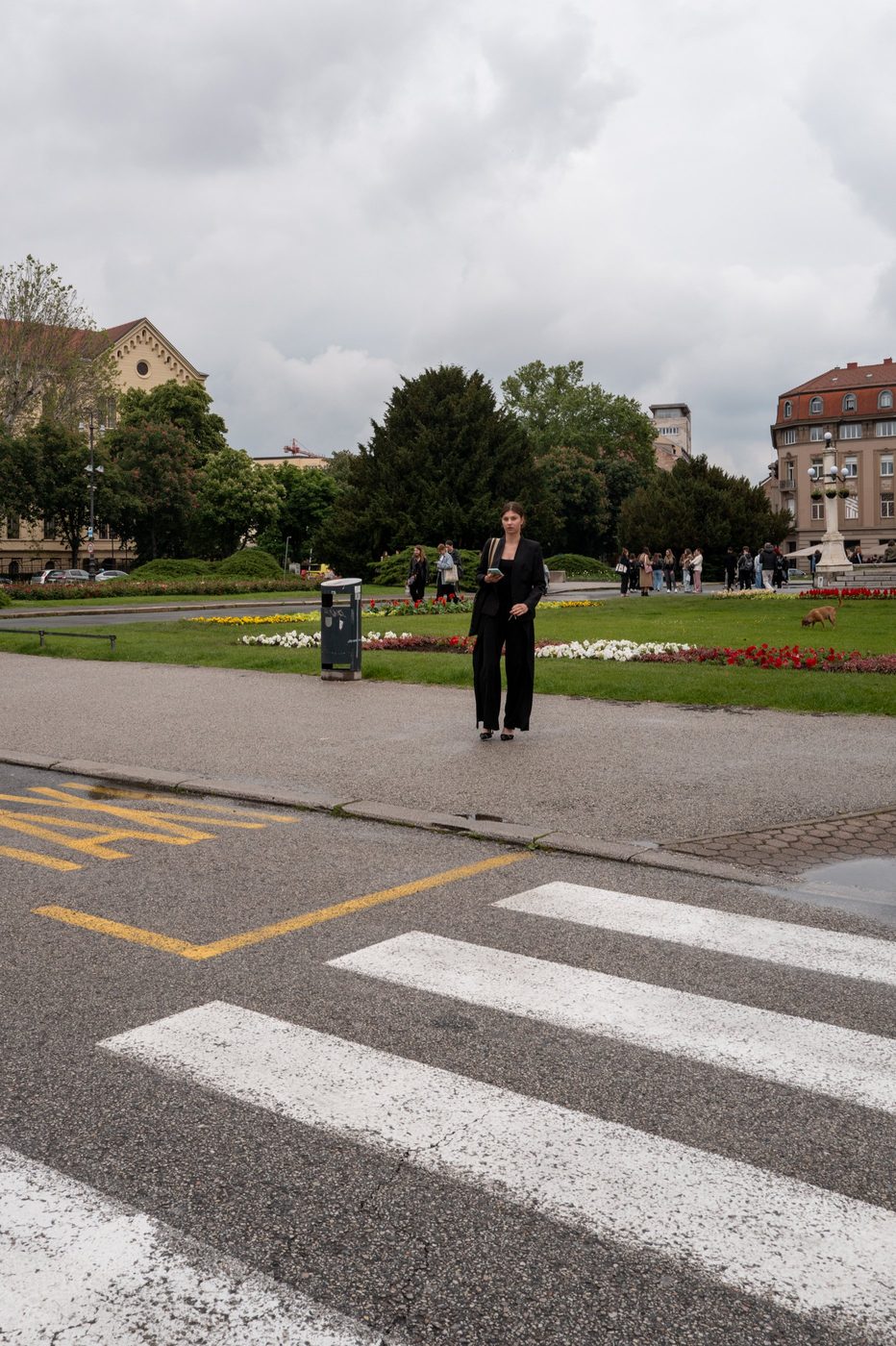 A woman in a black suit crossing near a flowering park, Zagreb