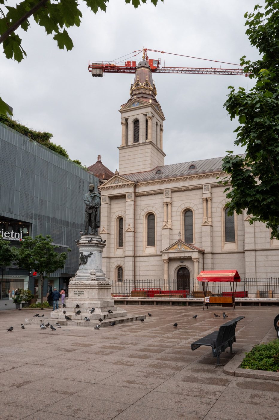 Bronze statue surrounded by pigeons in front of the church, crane in the background, Zagreb