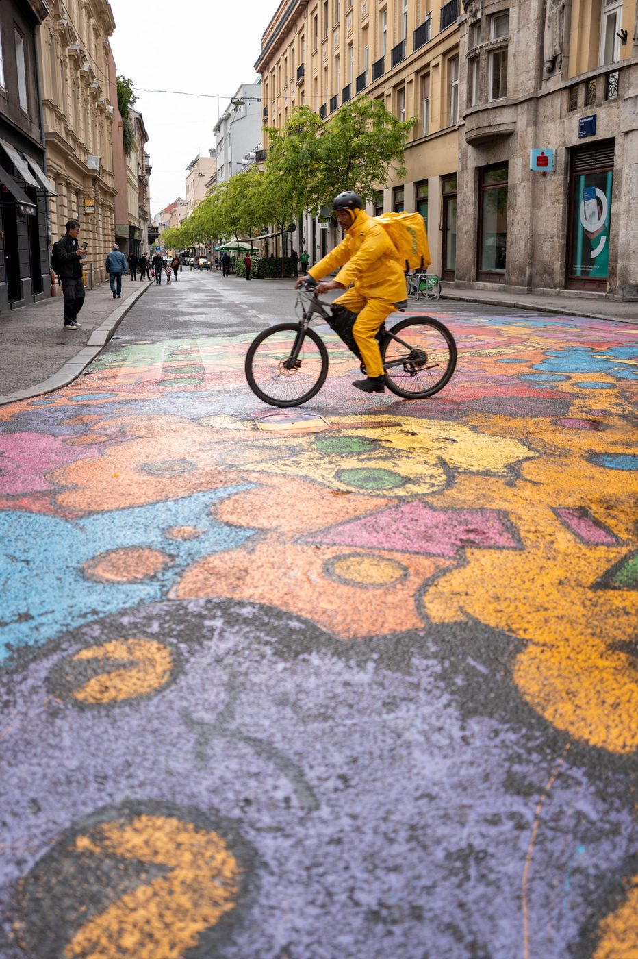 Bicycle delivery rider crossing a colorful mural painted on the pavement, Zagreb