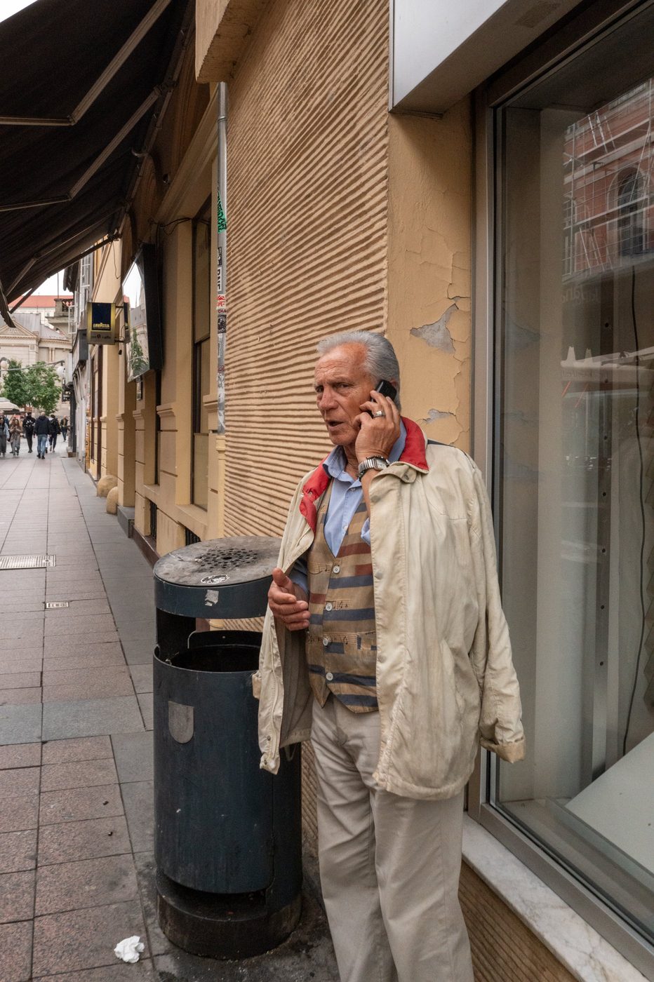 An elderly man on the phone leaning against a street trash can, Zagreb