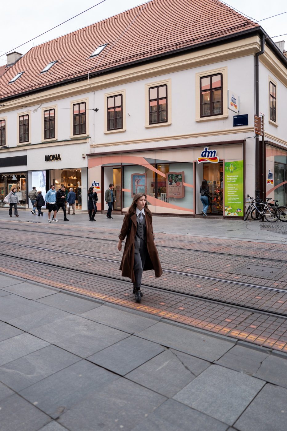 A passerby in a brown coat crossing the tram tracks, Zagreb