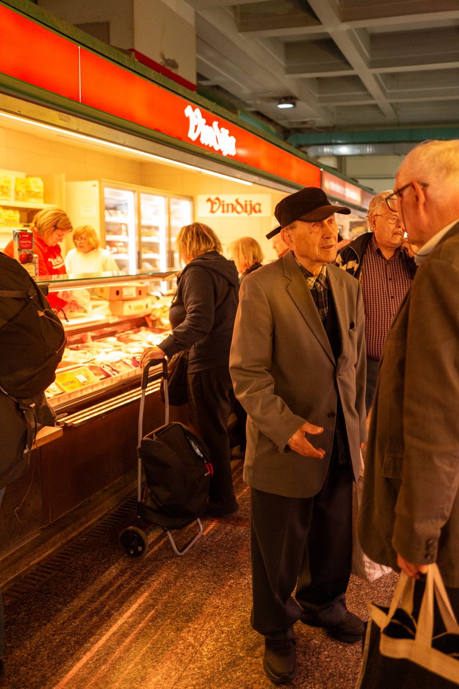 An elderly man in a flat cap chatting near the Vindija counter, Zagreb
