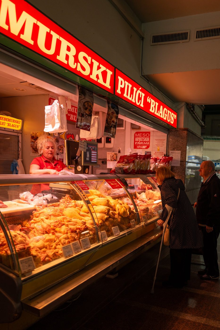 Stall of roasted poultry beneath a glowing red sign, Zagreb