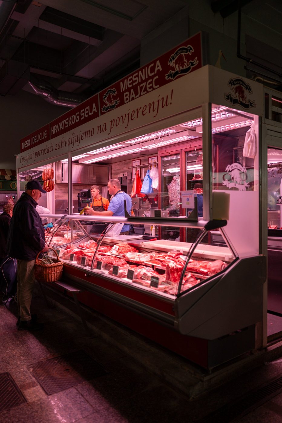 A customer with a basket in front of a butcher shop's refrigerated display, Zagreb