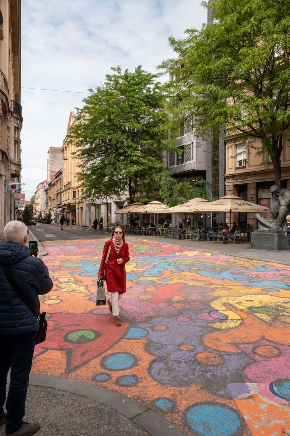 A woman in a red coat photographed against the colorful mural, Zagreb