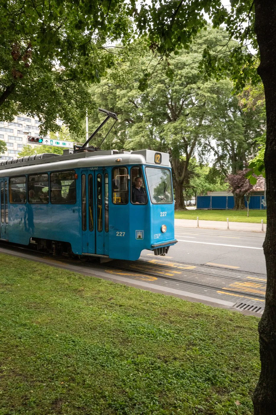 Tramway bleu numéro 227 circulant sous les frondaisons d'un parc, Zagreb