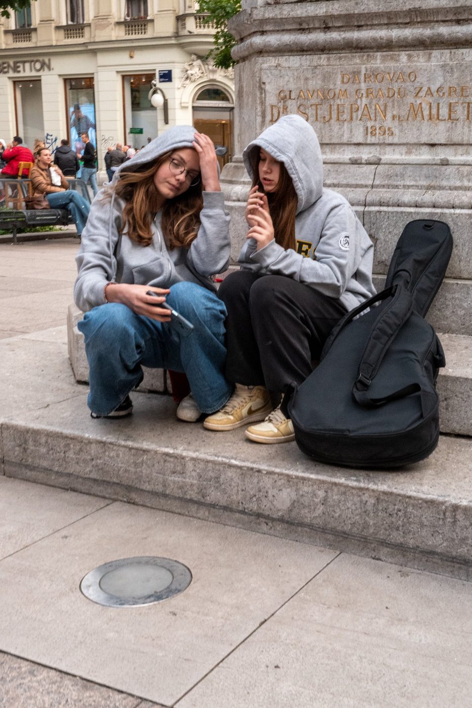 Two teenage girls in hoodies sitting near a guitar case, Zagreb