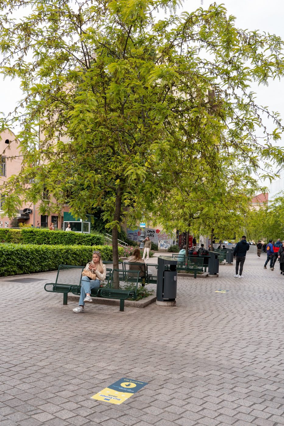 A young woman sitting alone under a tree on a public bench, Zagreb